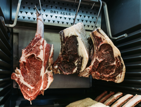 cuts of beef hanging from hooks in a dry aging fridge